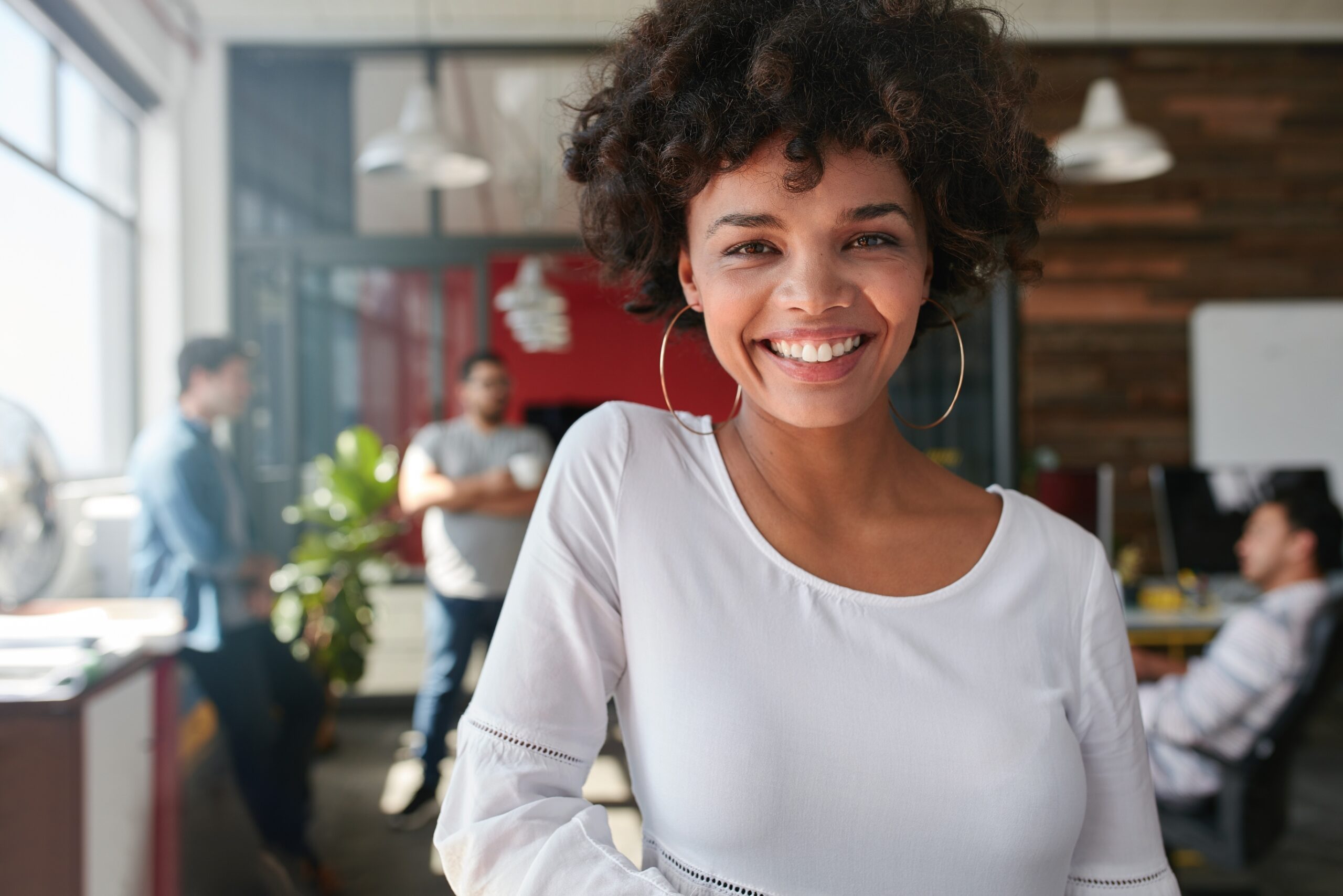 Portrait of smiling young african businesswoman with people in background.